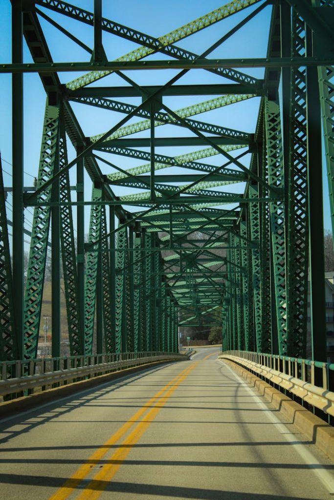 A detailed view of a green steel truss bridge with clear sky above, taken during the day.