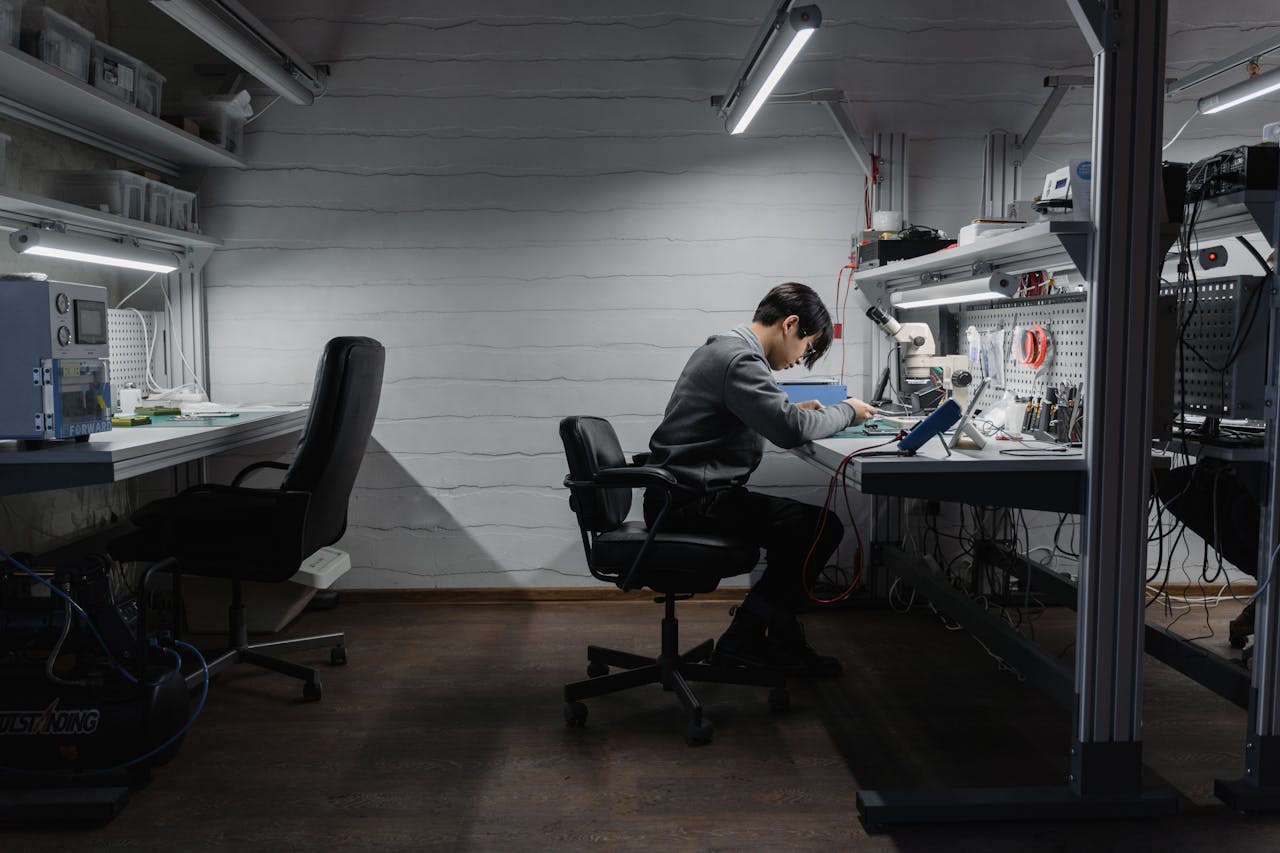 A man working on electronics at a well-lit workstation in an engineering lab.